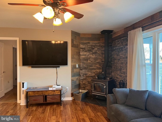 living area featuring a wood stove, ceiling fan, baseboards, and wood finished floors