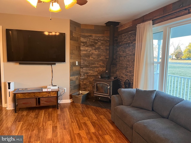 living area featuring a wood stove, ceiling fan, baseboards, and wood finished floors