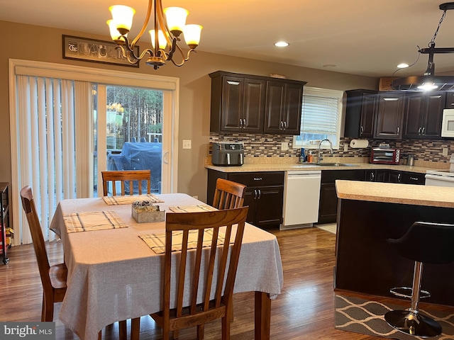 kitchen featuring tasteful backsplash, light countertops, a sink, wood finished floors, and white appliances