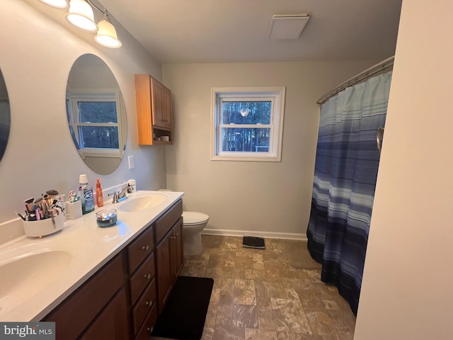 bathroom featuring toilet, a sink, baseboards, and double vanity