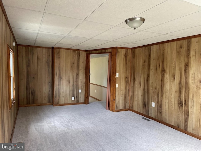 carpeted spare room featuring ornamental molding, visible vents, wooden walls, and baseboards