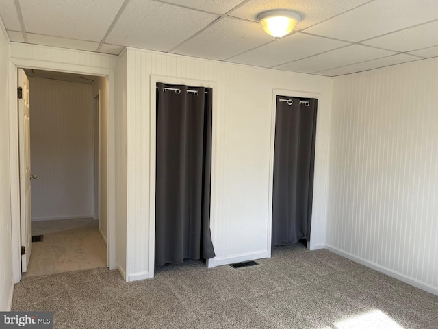 unfurnished bedroom with carpet floors, baseboards, visible vents, and a paneled ceiling