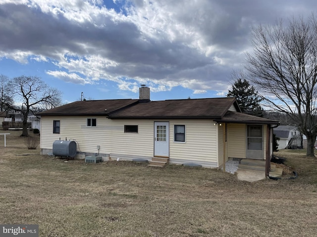 rear view of house featuring a chimney, a lawn, central AC unit, entry steps, and heating fuel