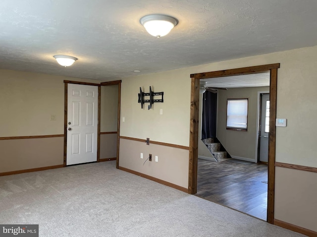 carpeted empty room featuring stairway, baseboards, and a textured ceiling