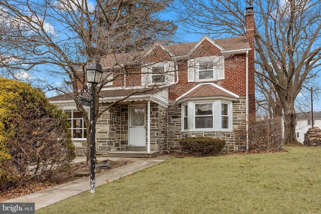 view of front of home with brick siding, stone siding, roof with shingles, a front lawn, and a chimney