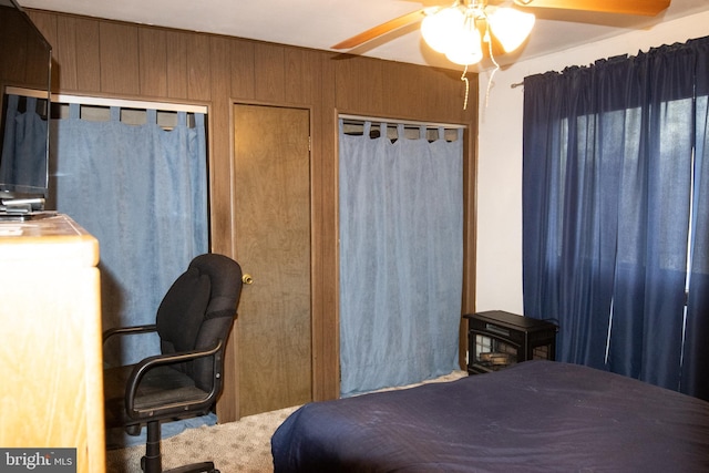 bedroom with multiple closets, wood walls, and ceiling fan