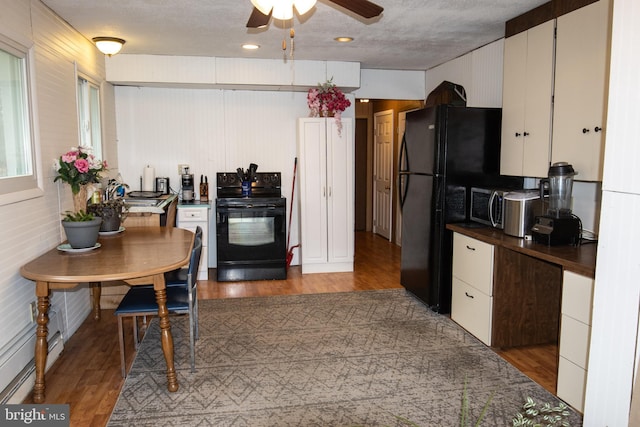 kitchen with dark countertops, white cabinetry, black appliances, and wood finished floors