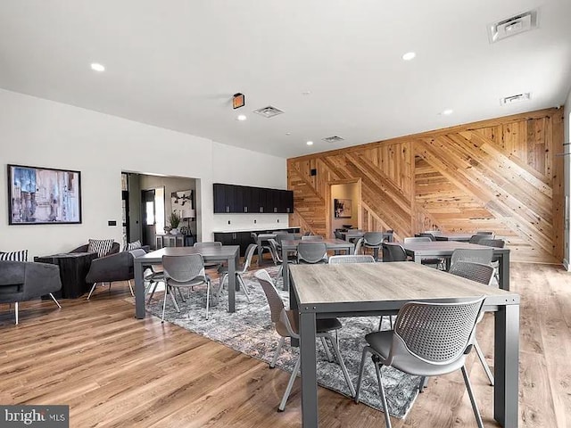 dining area featuring light wood finished floors, visible vents, and wood walls