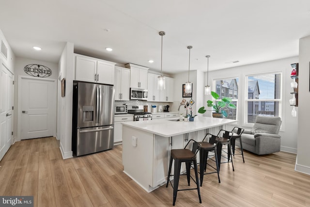 kitchen with stainless steel appliances, a sink, white cabinetry, light wood-style floors, and a kitchen bar