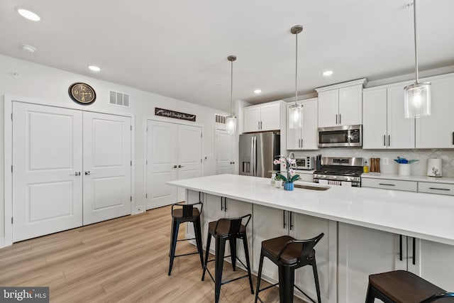 kitchen with stainless steel appliances, light wood-style floors, a sink, and a kitchen bar