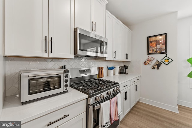 kitchen featuring light wood-style flooring, a toaster, light countertops, appliances with stainless steel finishes, and decorative backsplash