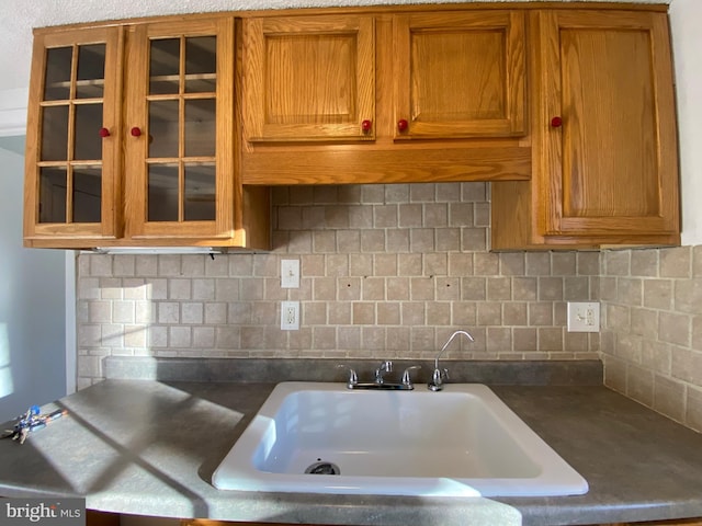 kitchen featuring brown cabinetry, glass insert cabinets, a sink, and tasteful backsplash