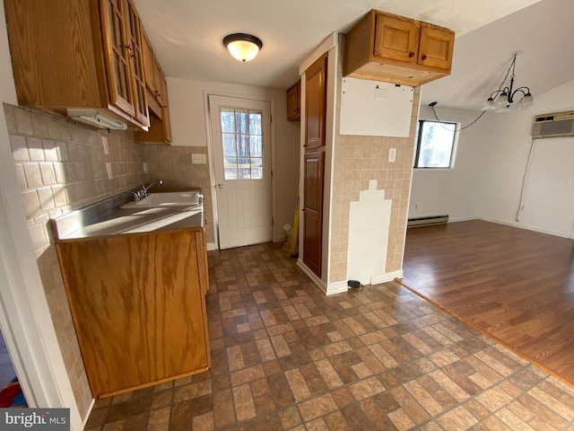 kitchen with a wall unit AC, a baseboard radiator, decorative backsplash, brown cabinetry, and a sink