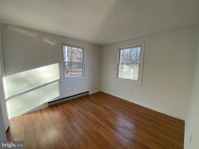 empty room with baseboards, a healthy amount of sunlight, baseboard heating, and wood finished floors