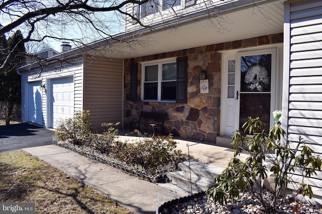 entrance to property featuring a garage, stone siding, aphalt driveway, and a chimney