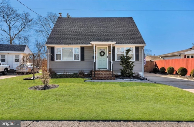 view of front facade with a shingled roof, a front yard, and fence