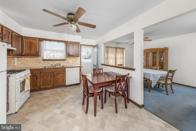 kitchen with white appliances, baseboards, decorative backsplash, under cabinet range hood, and a sink