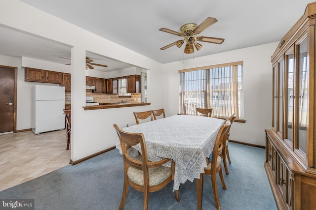 dining area featuring light carpet, a ceiling fan, and baseboards