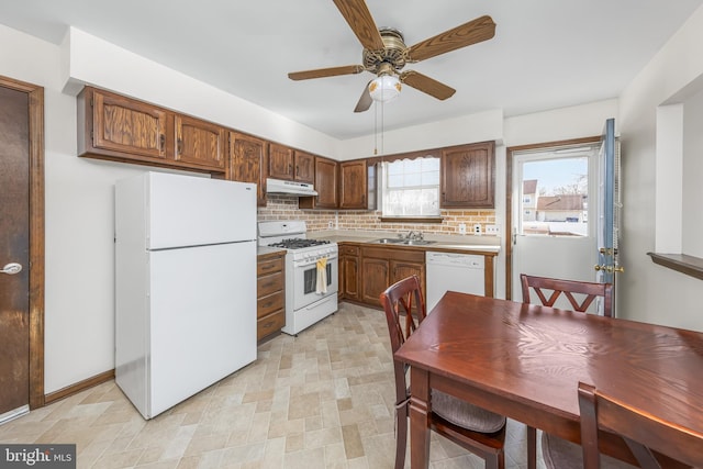 kitchen with white appliances, under cabinet range hood, decorative backsplash, and a sink