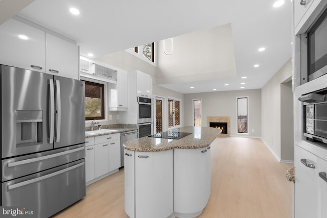 kitchen featuring a center island, a fireplace, stainless steel appliances, white cabinets, and a sink