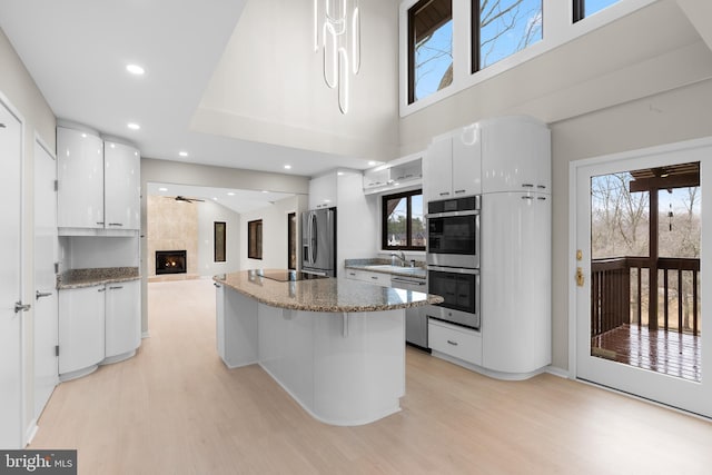 kitchen featuring light wood-style flooring, a large fireplace, a kitchen island, white cabinetry, and appliances with stainless steel finishes