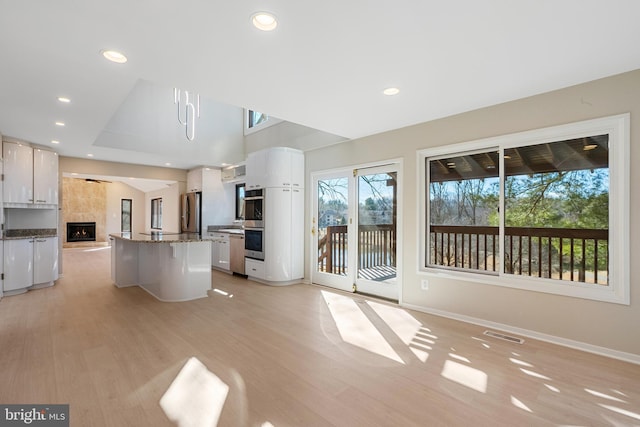 kitchen with a fireplace, appliances with stainless steel finishes, light wood-style floors, stone countertops, and white cabinets