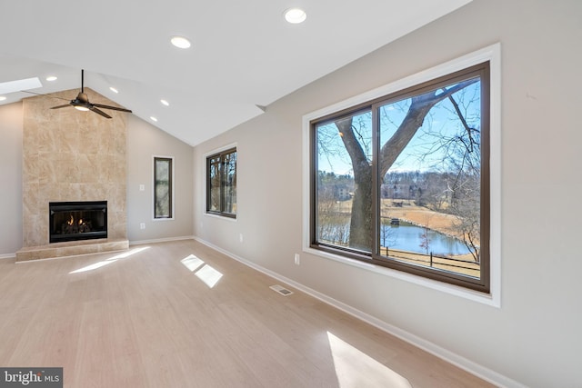 unfurnished living room featuring a tile fireplace, visible vents, light wood-style floors, vaulted ceiling, and baseboards