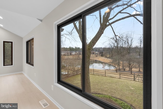 doorway featuring a water view, visible vents, vaulted ceiling, wood finished floors, and baseboards