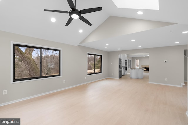 unfurnished living room with high vaulted ceiling, light wood-style flooring, recessed lighting, a skylight, and baseboards