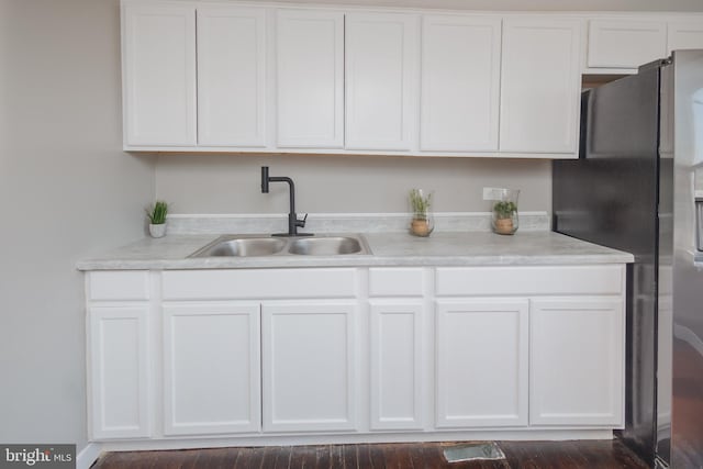 kitchen with freestanding refrigerator, white cabinetry, and a sink