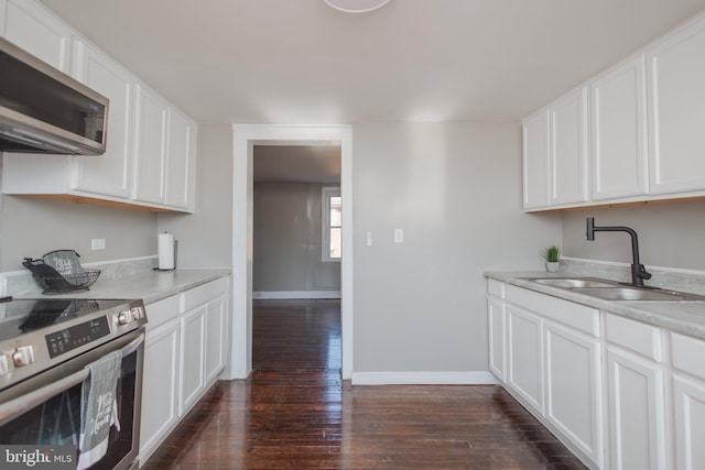 kitchen with a sink, baseboards, light countertops, appliances with stainless steel finishes, and dark wood-style floors