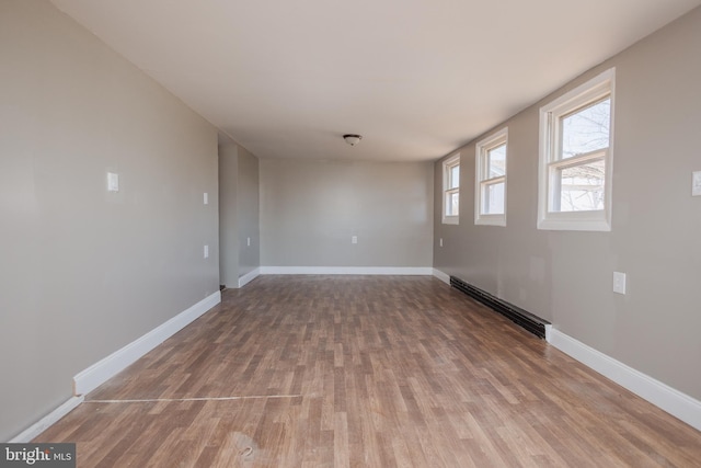 spare room with baseboards, baseboard heating, and wood finished floors