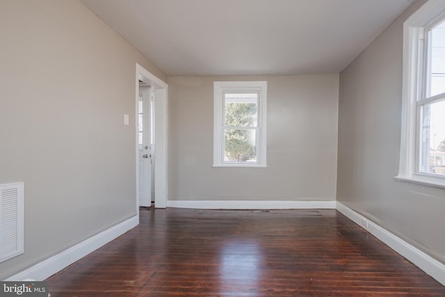 spare room featuring dark wood-style floors, visible vents, and baseboards