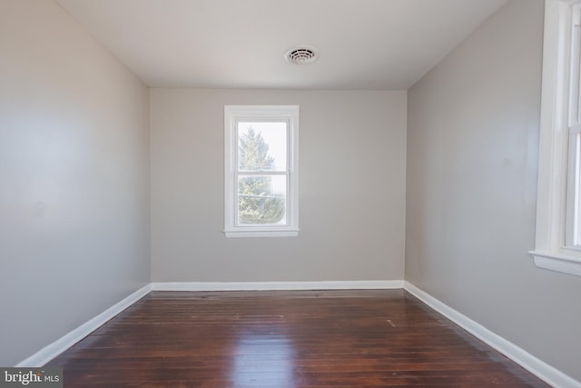 spare room with dark wood-style flooring, visible vents, and baseboards