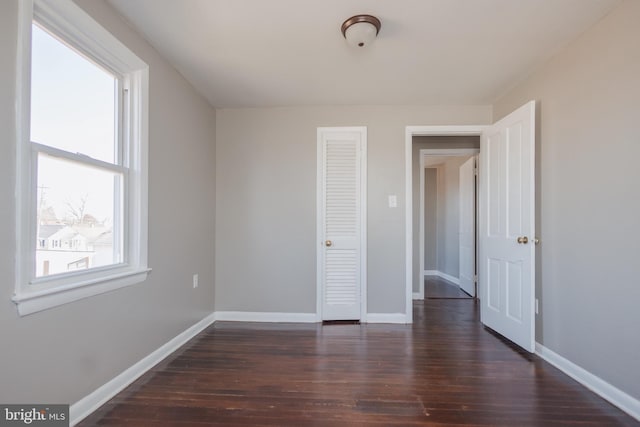 unfurnished bedroom with dark wood-style floors, a closet, and baseboards