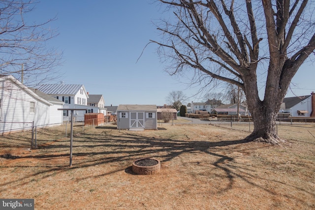 view of yard featuring an outdoor fire pit, an outdoor structure, fence, a residential view, and a shed