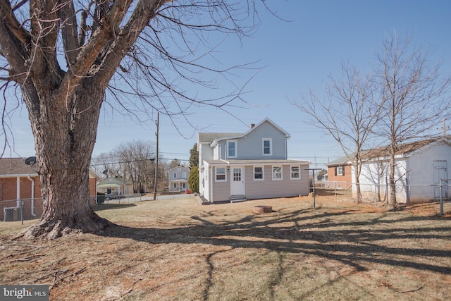 rear view of property with entry steps, fence, and a lawn