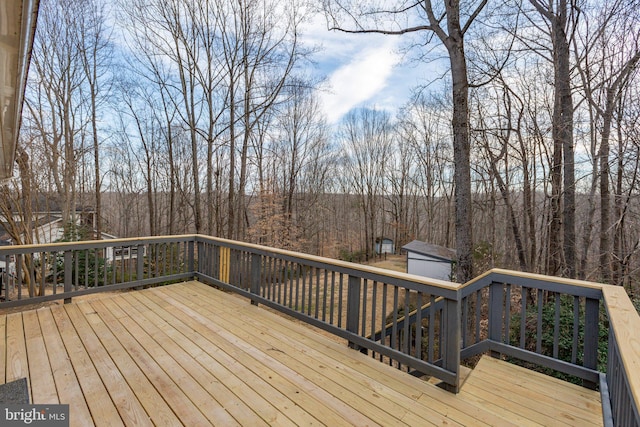 wooden terrace featuring a storage unit, a view of trees, and an outdoor structure