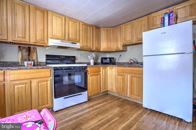 kitchen with under cabinet range hood, a sink, light wood-type flooring, freestanding refrigerator, and gas range oven