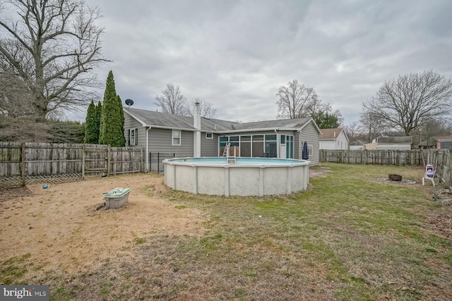 back of house featuring a fire pit, a lawn, a fenced in pool, a sunroom, and a fenced backyard