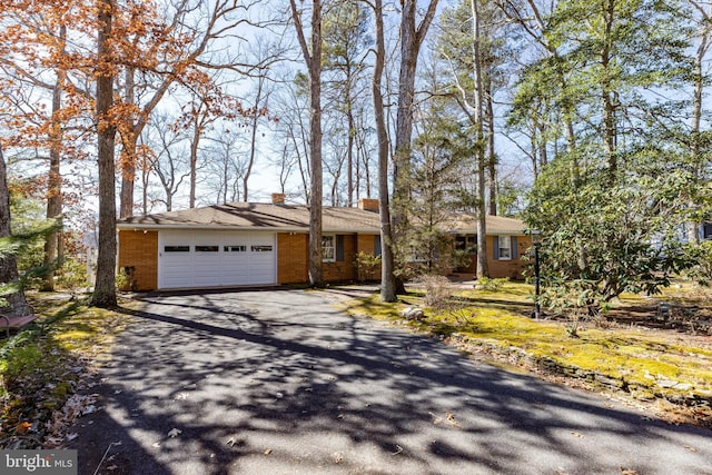 view of front facade with brick siding, driveway, a chimney, and an attached garage