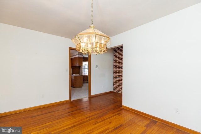 unfurnished room with baseboards, hardwood / wood-style flooring, and a notable chandelier