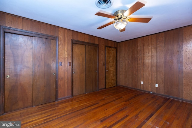 unfurnished bedroom with hardwood / wood-style floors, wooden walls, visible vents, and multiple closets