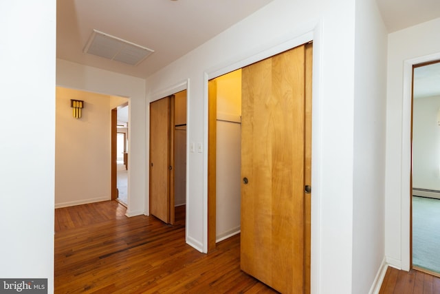 hallway with a baseboard heating unit, wood-type flooring, visible vents, and baseboards