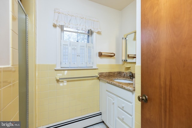 bathroom featuring a shower with shower door, a wainscoted wall, vanity, tile walls, and baseboard heating