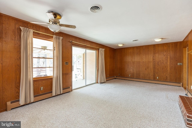 spare room featuring light carpet, a baseboard radiator, wooden walls, and visible vents