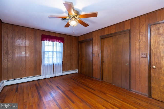 unfurnished bedroom with multiple closets, ceiling fan, wooden walls, and hardwood / wood-style floors