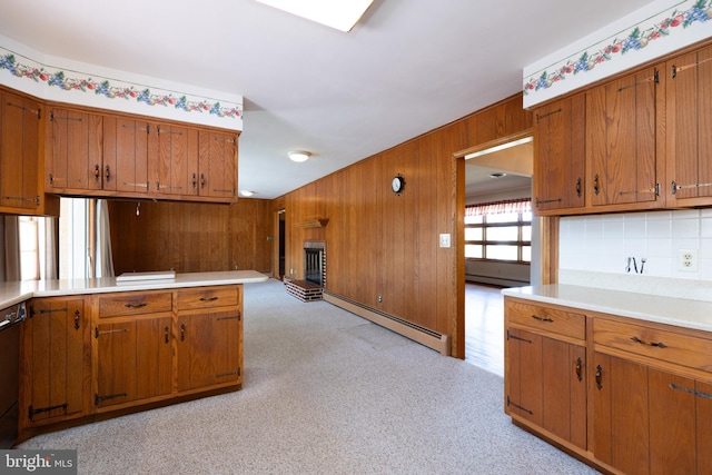 kitchen featuring wooden walls, brown cabinetry, light countertops, a brick fireplace, and a baseboard heating unit