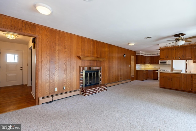 unfurnished living room with light colored carpet, a fireplace, wooden walls, and baseboard heating