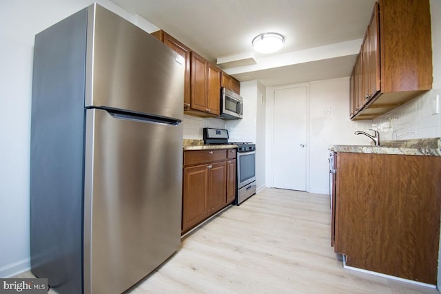 kitchen featuring appliances with stainless steel finishes, brown cabinets, light wood finished floors, and decorative backsplash